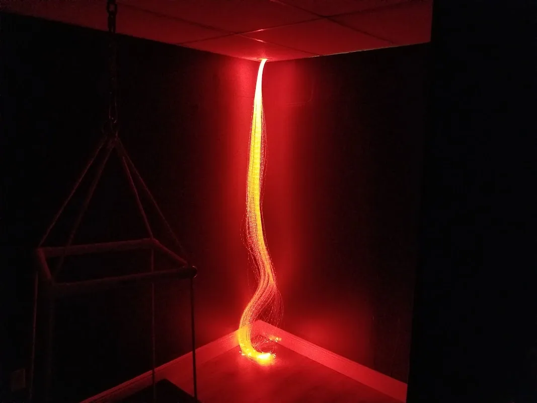 Close-up of a fiber-optic strand light in the sensory room with warm red ambient lighting, used to support visual and tactile sensory regulation